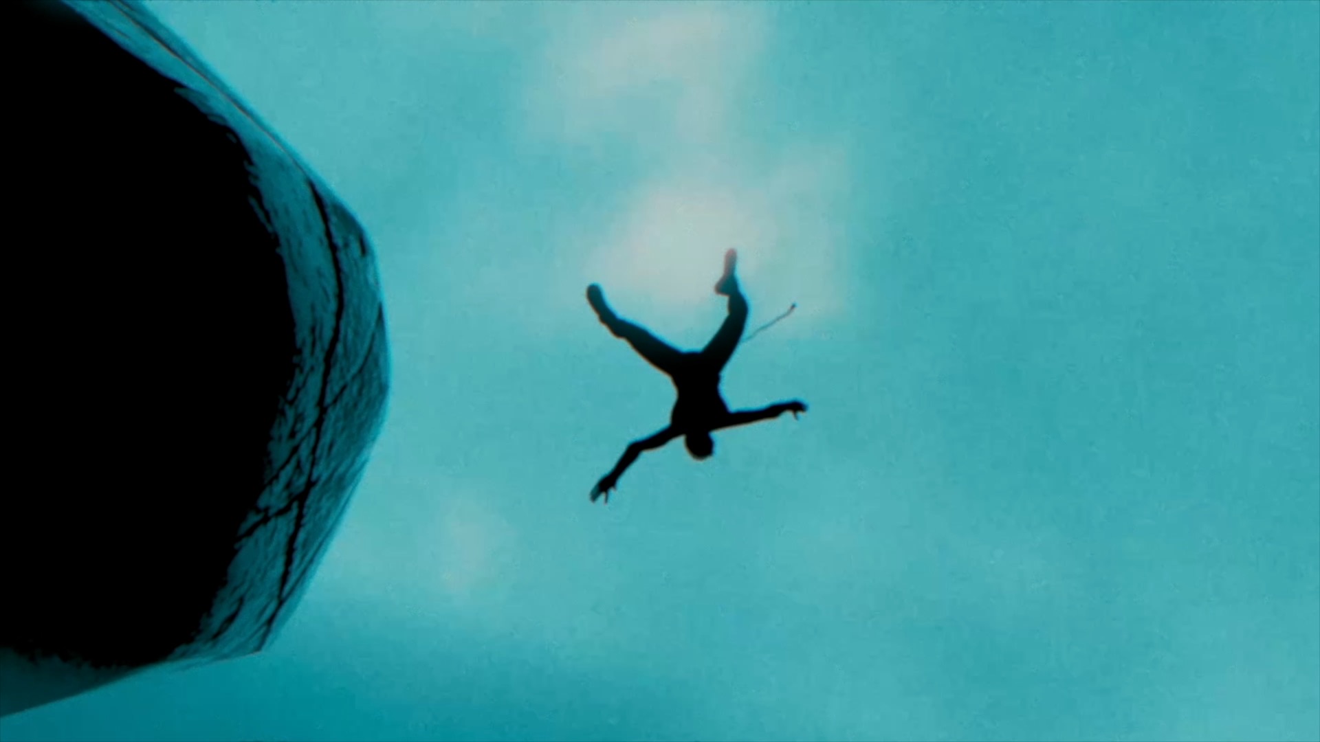A climber falling through open sky past the edge of a cliff. Film still.