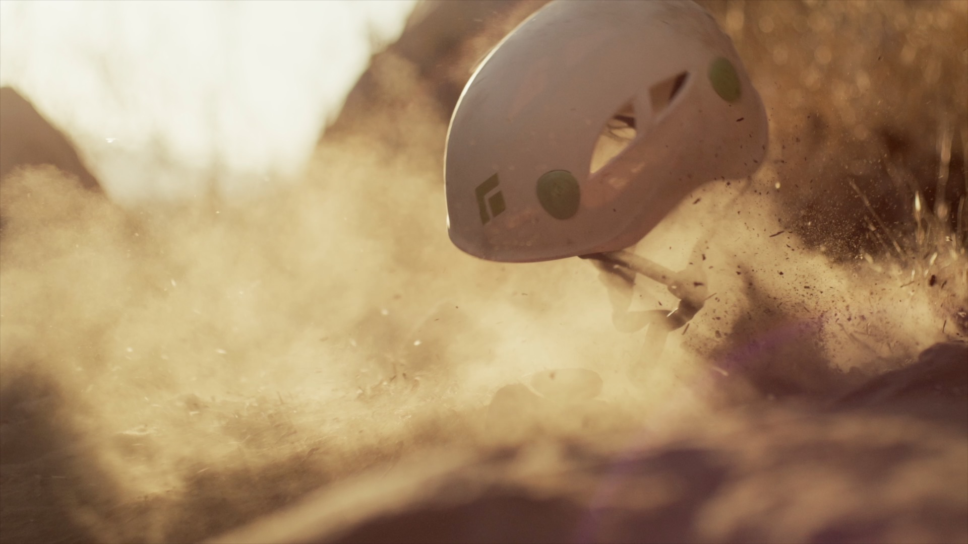 A white Black Diamond climbing helmet hitting the ground in a burst of dust. Film still.