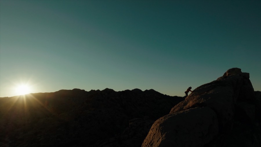 A climber on a summit as the sun sets. Film still.