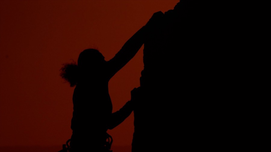 Andrea reaching for a hold in silhouette at sunset. Film still.